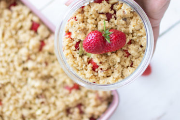 Erdbeer-Rhabarber-Crumble fertig fotografiert im Glas mit händen umklammert.
